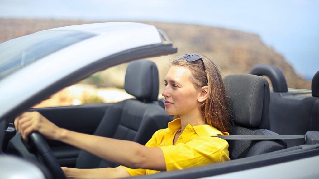 Giovane donna al volante di un’auto cabrio su strada panoramica.